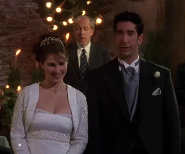 Ross and Emily stand at their wedding, dressed elegantly, with a minister in the background.