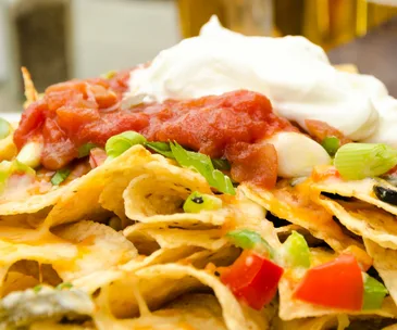 A plate of nachos topped with salsa, sour cream, chopped green onions, and diced tomatoes.