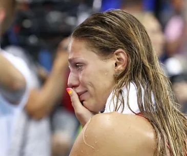 Swimmer with wet hair holding a towel, emotional and tearful after competition.