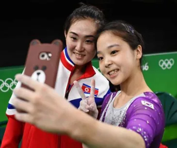 North and South Korean gymnasts smiling together, taking a selfie during the Olympics, symbolizing unity.