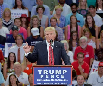 Donald Trump speaking at a rally in Wilmington, North Carolina, with a crowd behind him.
