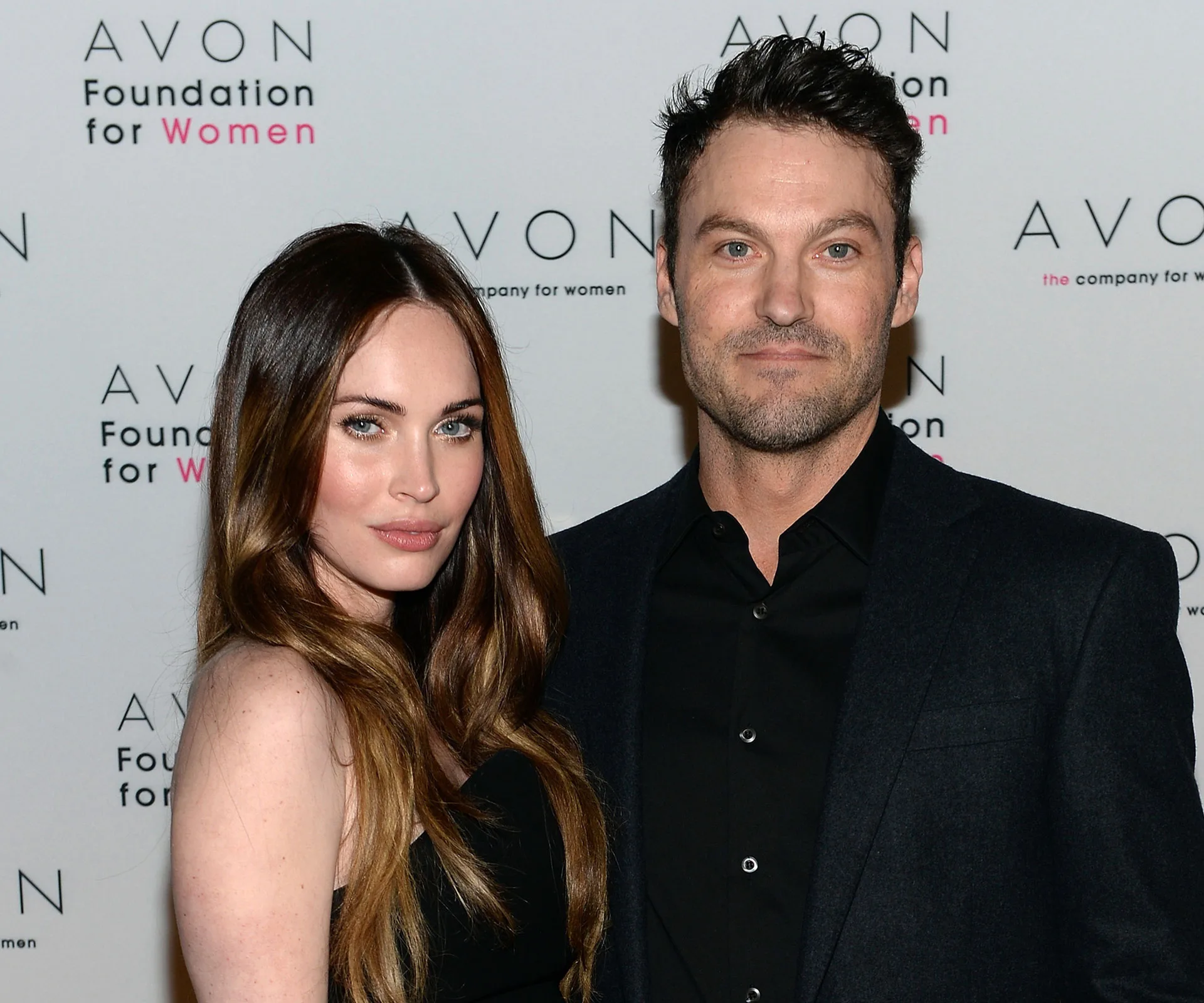 A couple poses together at an Avon event, with a branded backdrop behind them.