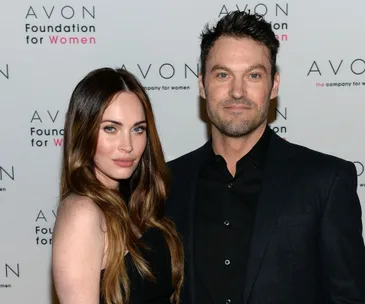 A couple poses together at an Avon event, with a branded backdrop behind them.