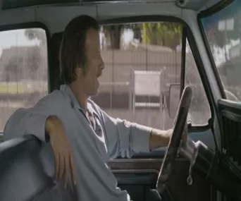 A man driving a truck looks out the window, casually resting his arm on the seat.