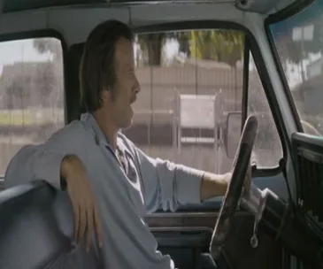 A man driving a truck looks out the window, casually resting his arm on the seat.