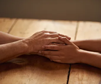 Hands of an adult and child gently holding each other on a wooden table.