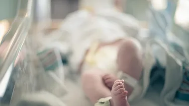 A newborn baby lying in a hospital crib, focus on tiny feet, wrapped in a diaper and hospital blankets.