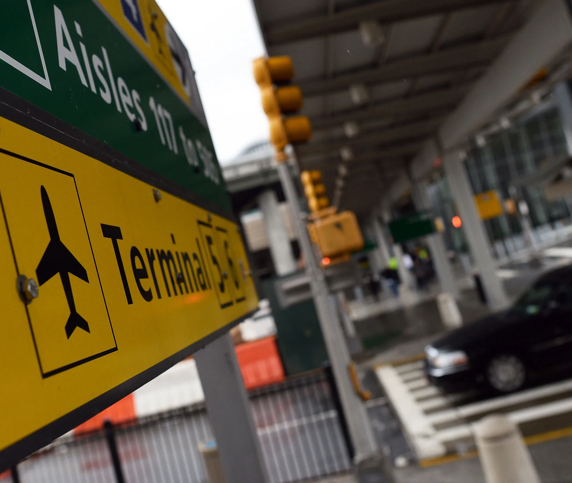 Sign for Terminal 5 at JFK Airport, with traffic lights and a car in the background, creating a busy scene.