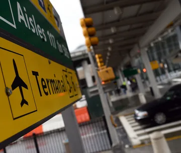 Sign for Terminal 5 at JFK Airport, with traffic lights and a car in the background, creating a busy scene.