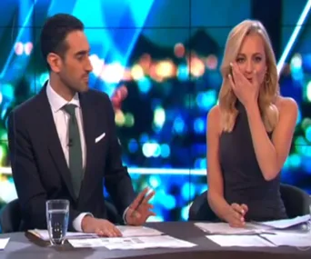 Two TV hosts at a news desk; one appears emotional, covering their mouth with a hand.