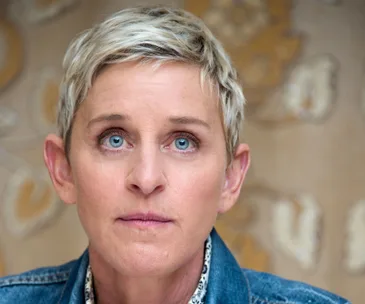 A person with short blonde hair and a denim jacket looking upwards with a contemplative expression.