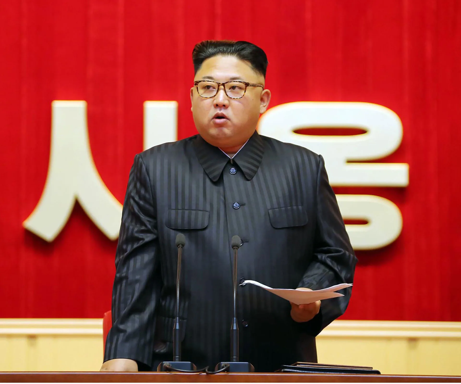 Leader delivering a speech at a podium against a red background.