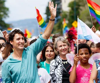 Justin Trudeau waves amidst a crowd at a pride parade, people holding rainbow flags.