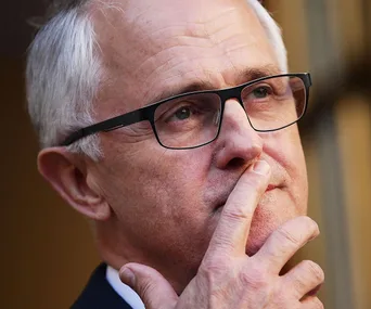 A thoughtful man with glasses, fingers on his chin, gazing upward.