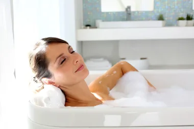 Woman relaxing in a bubble bath, eyes closed, enjoying the warm water in a bright bathroom.
