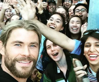Actor with fans taking a selfie at a crowded event, smiling broadly; lively atmosphere.