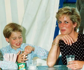 A young boy and Princess Diana sit at a table; the boy opens a can while Princess Diana smiles, with drinks nearby.