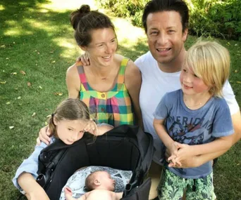 A smiling family of five in a garden, with two adults and three children; one child is in a stroller.