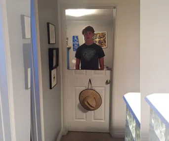 Teen stands behind a half-door cut-out with a hat hanging on it, showing creative punishment by parents.