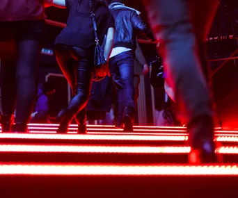 People walking up illuminated red stairs, viewed from below.