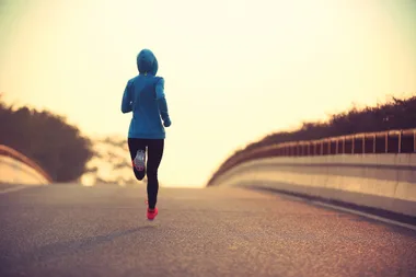 A person in a blue hoodie running on an empty road at sunrise.