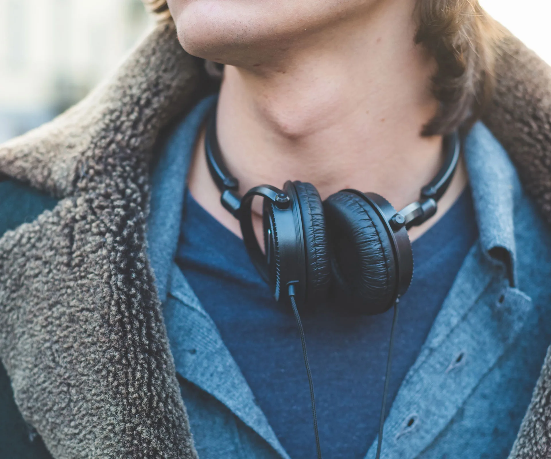 A person wearing a shearling coat and headphones around their neck.