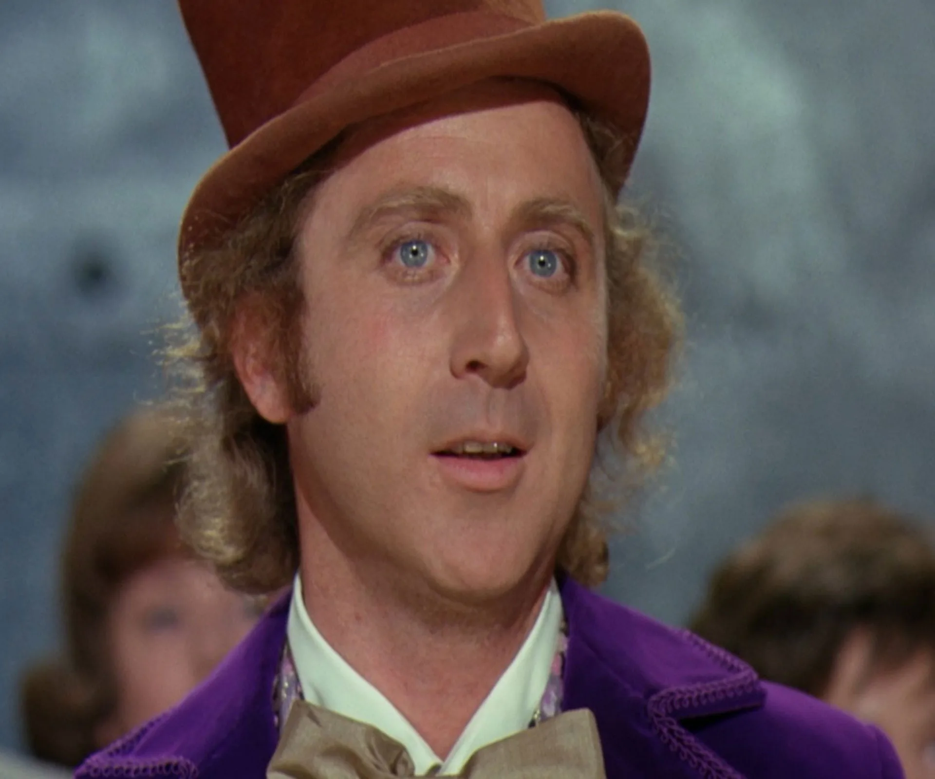 Gene Wilder as Willy Wonka, wearing a brown top hat and purple coat, with a thoughtful expression.