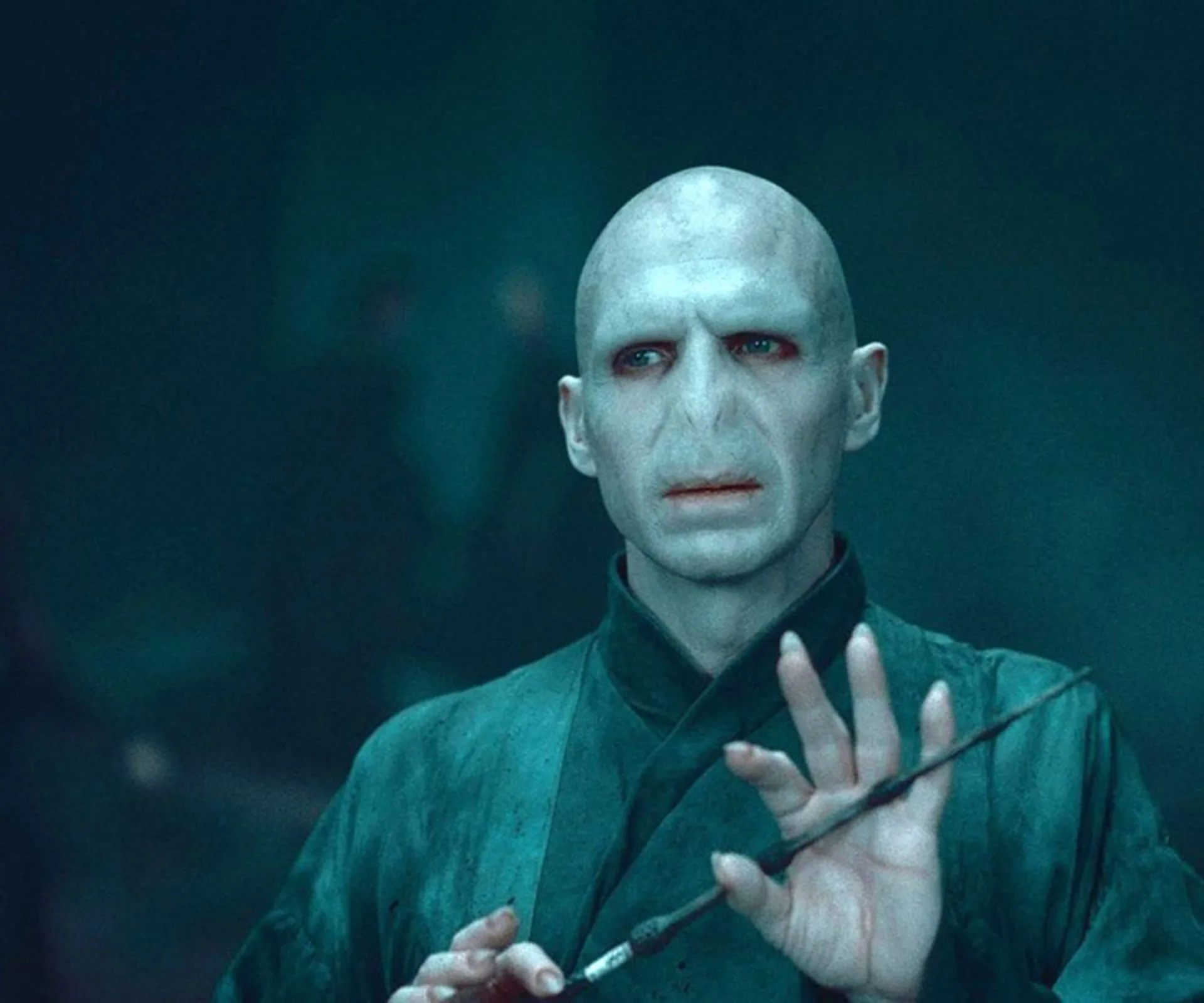 Character resembling Voldemort from Harry Potter series holding a wand, in a dimly lit, shadowy setting.