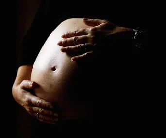 A pregnant belly cradled by two hands against a dark background.
