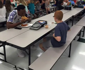 A man and a boy sit across from each other in a cafeteria, sharing lunch and conversation.