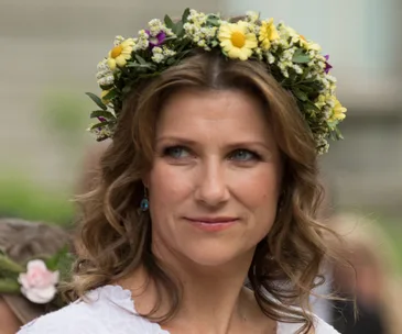 A woman wearing a floral crown with a thoughtful expression.