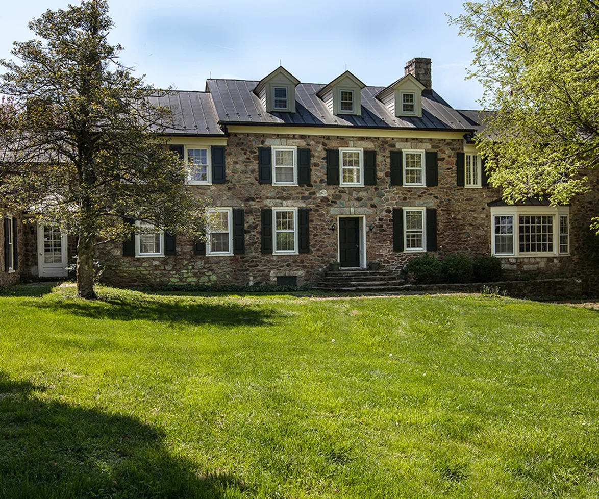 "Front view of Elizabeth Taylor's historic Virginia farmstead, featuring a stone facade, black shutters, and lush greenery."