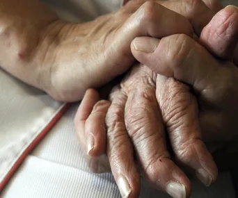 Elderly hands clasped together, symbolizing support and care.