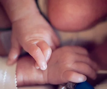 Close-up of a newborn's tiny hand grasping an adult finger, displaying delicate skin and small fingernails.