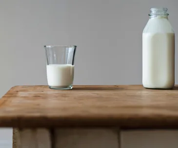 Glass and bottle of milk on a wooden table against a plain background.