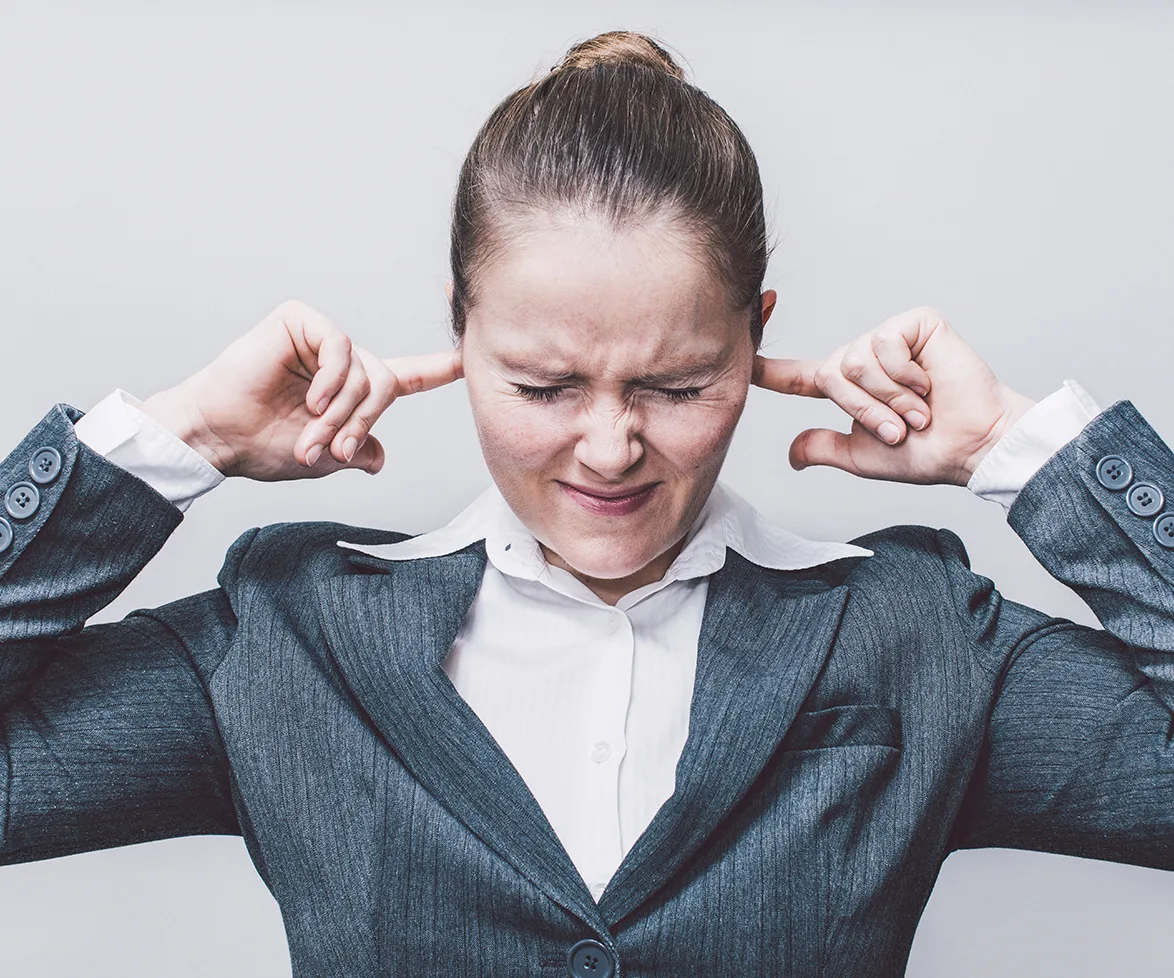 Woman in a suit covering her ears with fingers, eyes closed in discomfort.