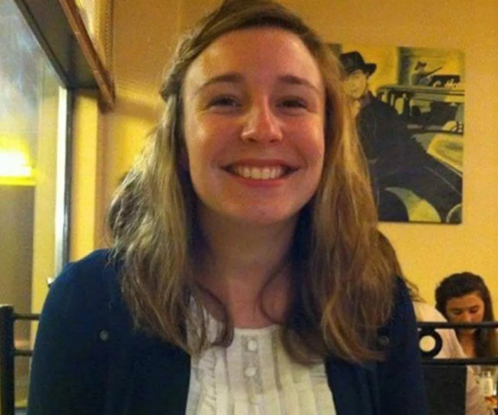 A smiling woman with long hair sitting in a cafe, with a painting in the background.