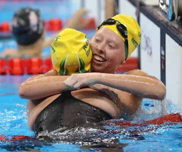 Australian swimmer in yellow cap celebrates winning gold at Rio 2016 Paralympics, hugging teammate in the pool.