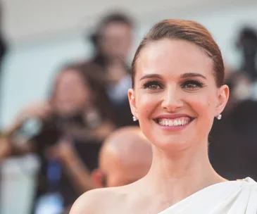 Smiling woman in a white dress at an outdoor event with a blurred crowd in the background.