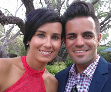A smiling couple taking a selfie outdoors, with trees in the background.