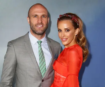A couple posing together; a man in a gray suit with a striped tie and a woman in a bright red dress with a headpiece.