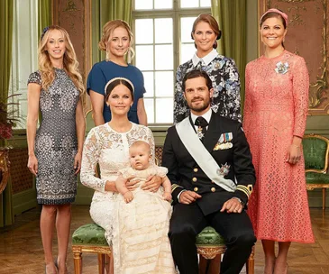 Royal family at Prince Alexander of Sweden's christening; adults stand, parents seated with baby. Elegant attire in ornate room.
