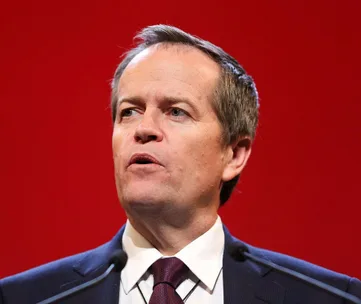 Man in a suit and tie speaking at a podium against a red background.