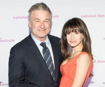 A man in a suit and a woman in a red dress smiling at an event, standing together against a backdrop.