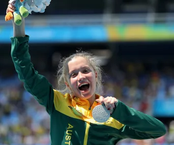Teen Paralympic athlete celebrates with a silver medal, wearing a green and yellow tracksuit, smiling broadly.