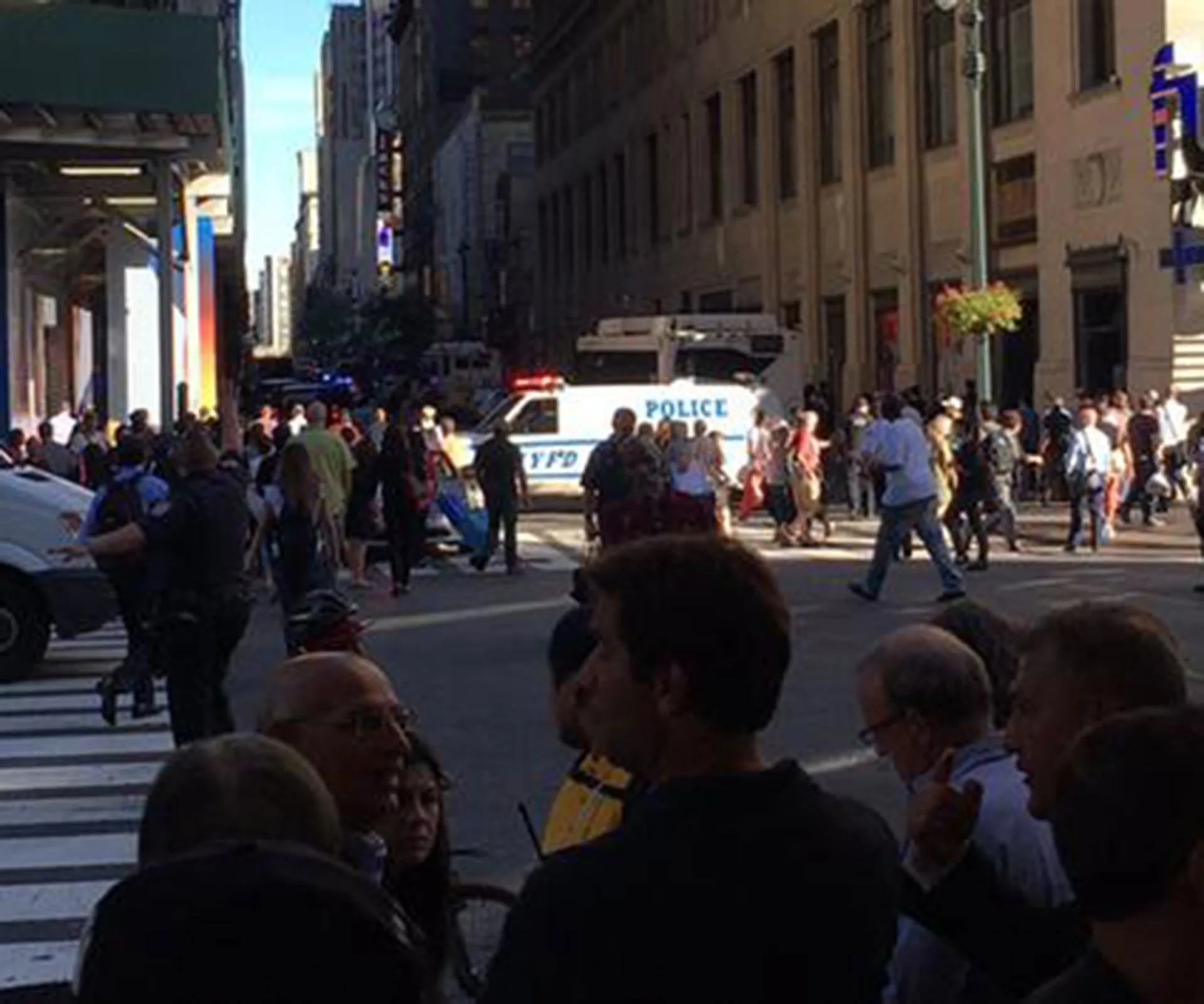 Crowd and police presence at a busy city street corner with an NYPD vehicle in the background.