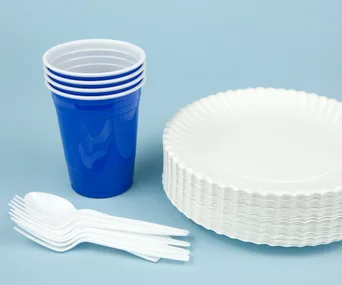 Stack of white plastic plates, blue cups, and white cutlery on a light blue background.
