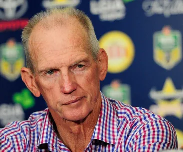 Man in a checked shirt at a press conference with a serious expression.