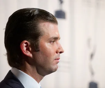 Profile view of a man in a suit with slicked-back hair at an event.