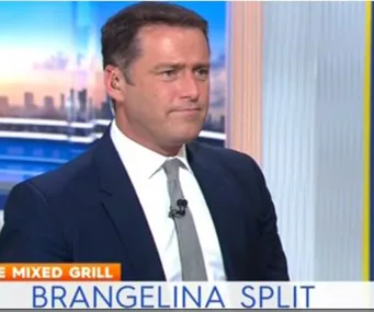 TV host discusses the Brangelina split on a news segment, looking serious on set with city skyline in the background.